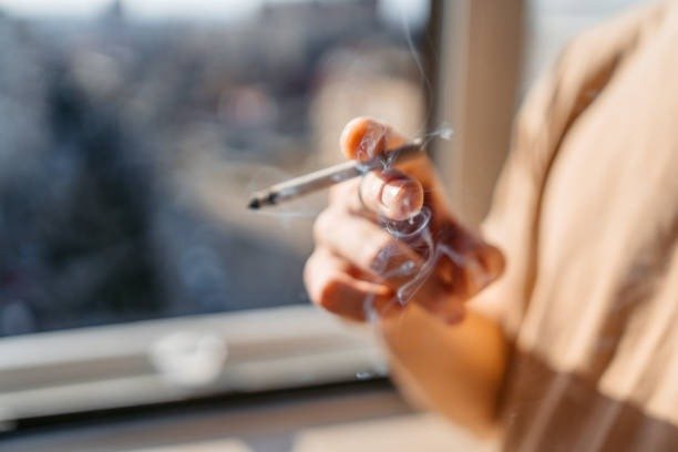 Young man smoking a cigarette by the window at home